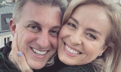 Close-up de mulher loira e homem grisalho sorrindo, faces próximas, mão toca rosto