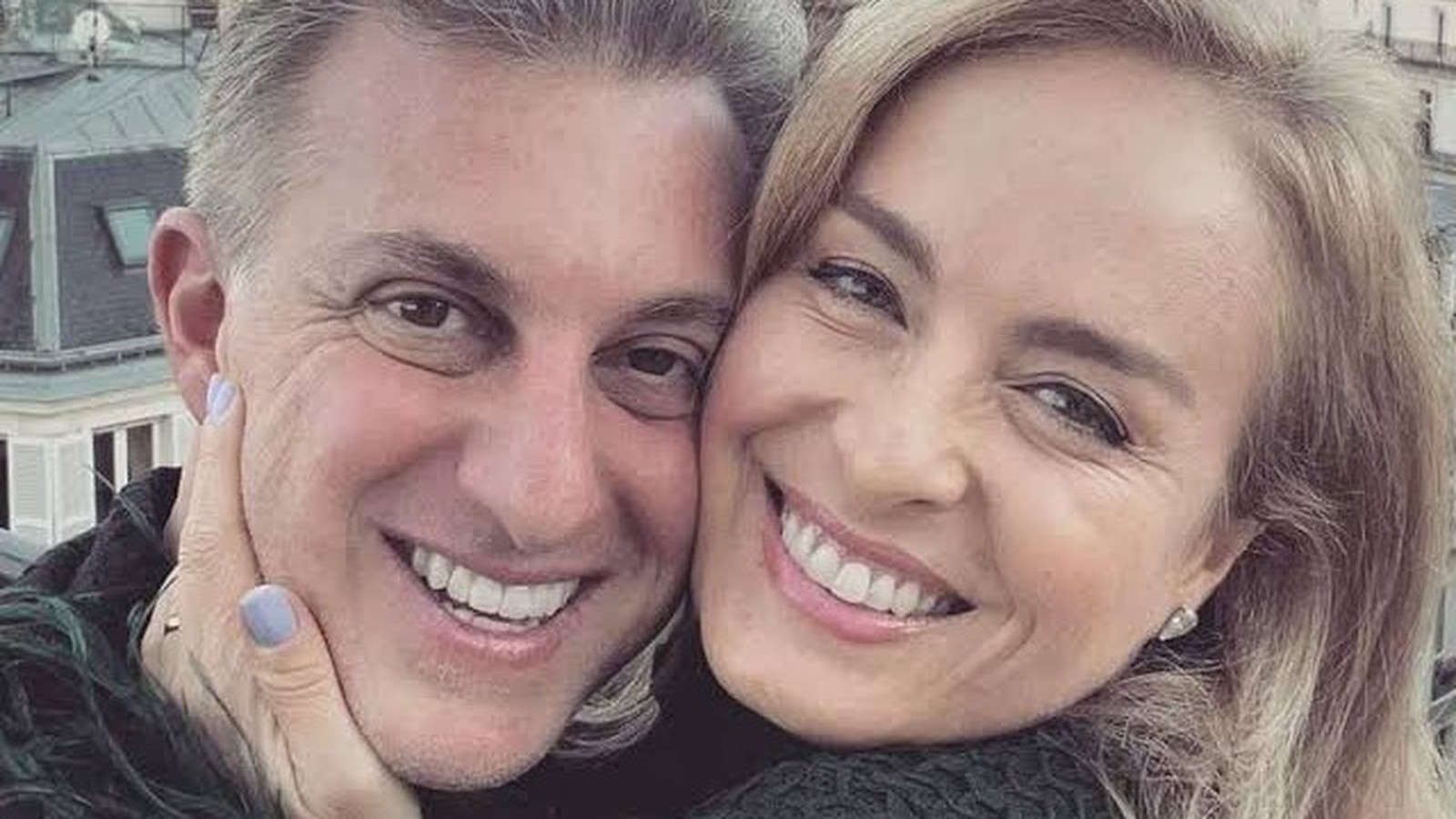 Close-up de mulher loira e homem grisalho sorrindo, faces próximas, mão toca rosto