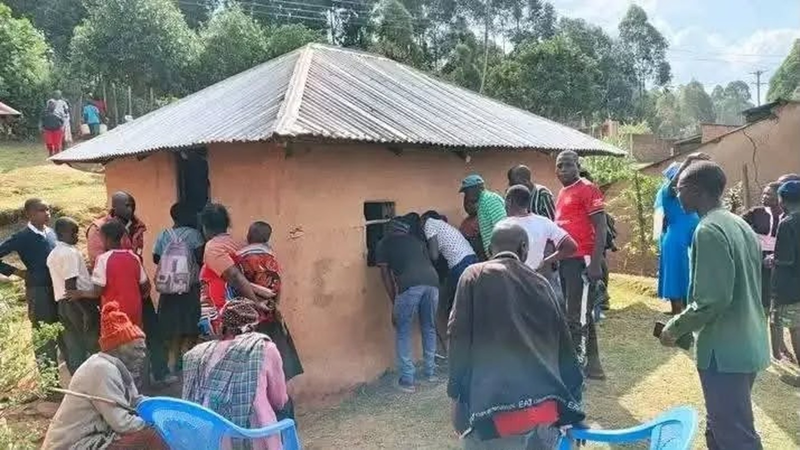 Multidão observa abertura em parede de casa simples, com telhado de zinco