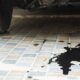 Mancha de óleo escura e grande no chão de azulejos claros, sob a roda e chassi de um carro