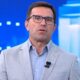 Rodrigo Bocardi, de óculos, camisa azul e paletó cinza, falando em estúdio de TV