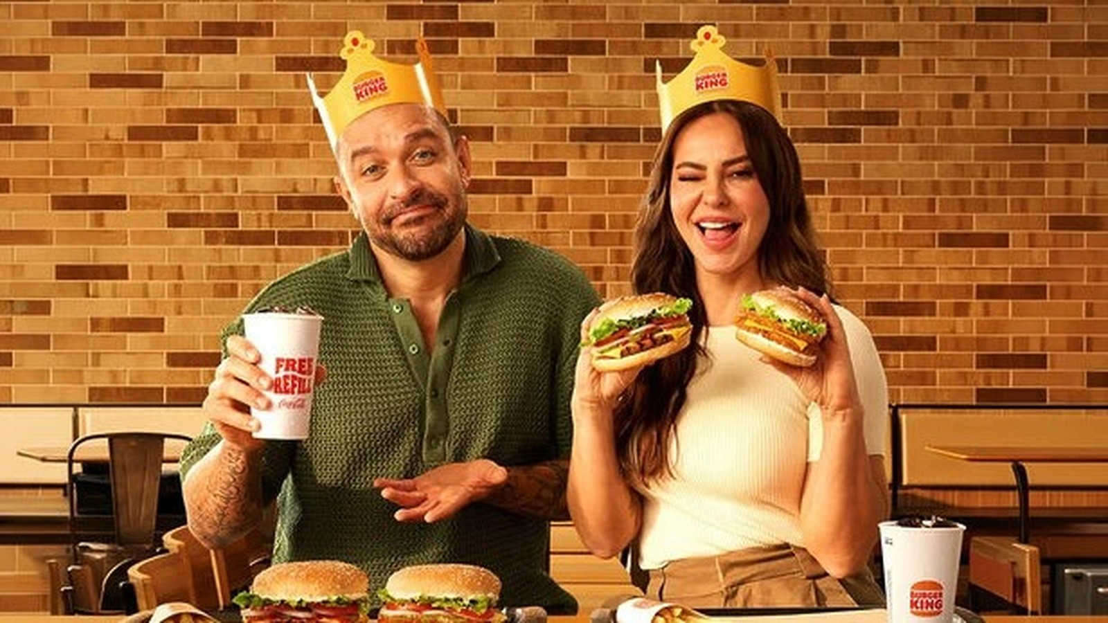 Homem e mulher com coroas Burger King seguram hambúrgueres e copo de refrigerante "FREE REFILL"