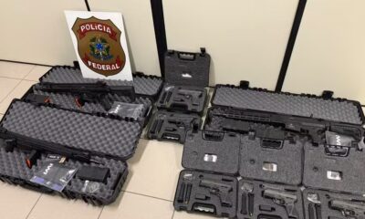 Várias armas de fogo, incluindo fuzis e pistolas, em estojos abertos e escudo da Polícia Federal