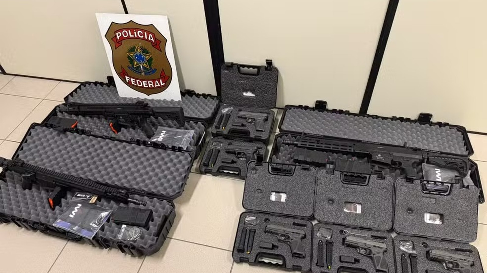 Várias armas de fogo, incluindo fuzis e pistolas, em estojos abertos e escudo da Polícia Federal