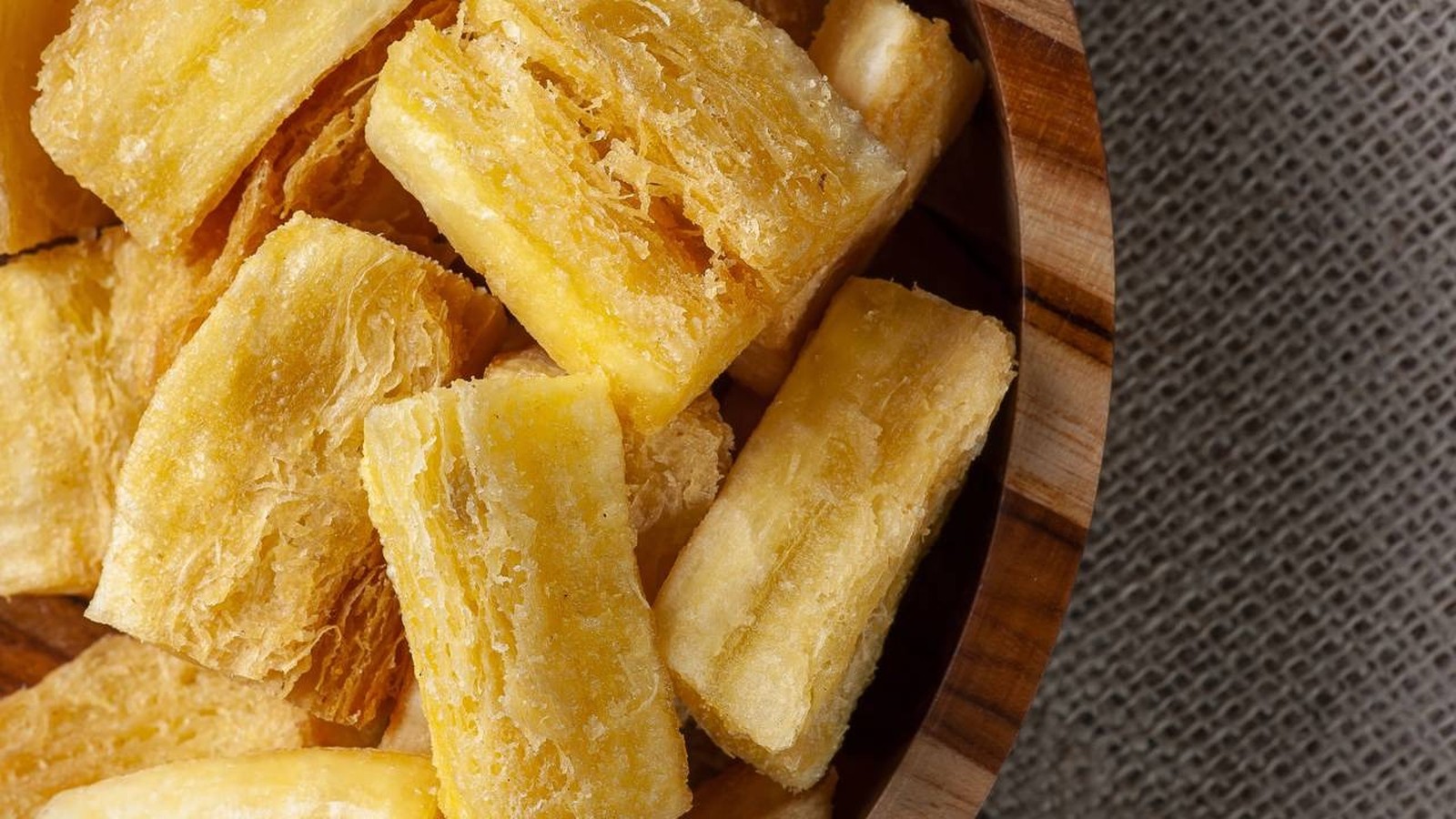 Aipim frito dourado e crocante em tigela de madeira sobre um tecido rústico