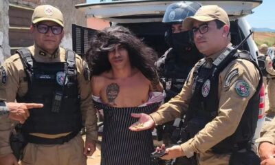 Dois policiais fardados e um homem preso com cabelos longos, camisa listrada, exibem munição