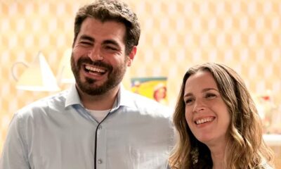 Thiago Lacerda e Vanessa Lóes sorrindo lado a lado, em close-up, com fundo claro