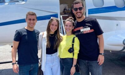 Quatro jovens sorrindo em frente a um jato particular branco e azul