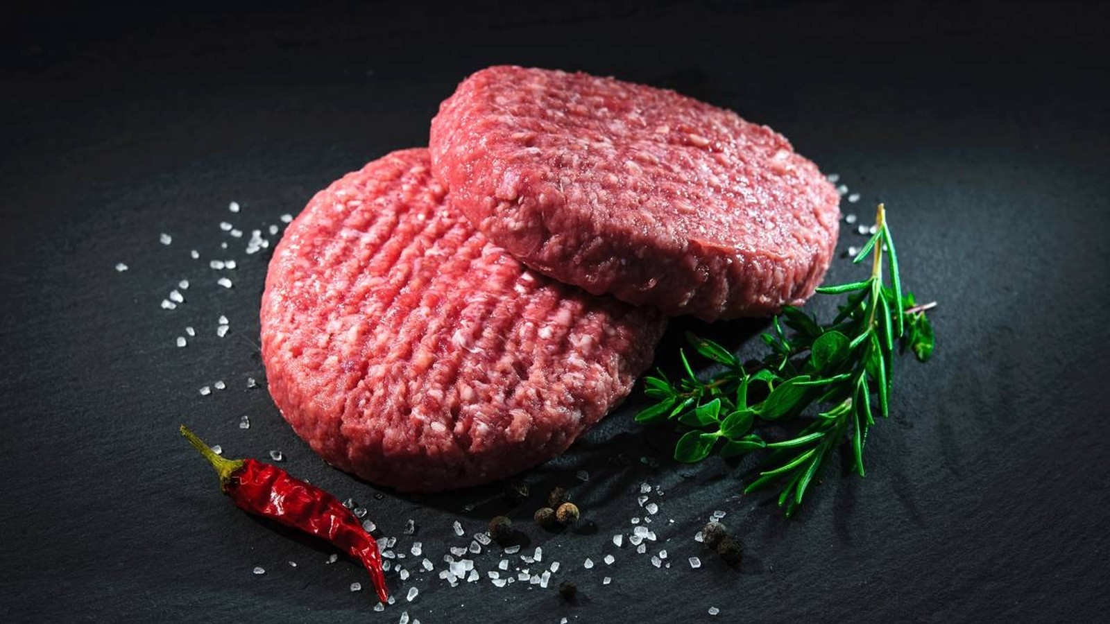 Duas hambúrgueres de carne crua com sal, pimenta preta, alecrim, tomilho e pimenta vermelha