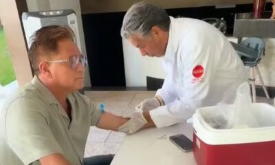 Leonardo, de óculos, tem sangue coletado do braço por profissional de jaleco branco