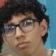 Close-up de jovem com cabelo escuro encaracolado e óculos, olhando para o lado