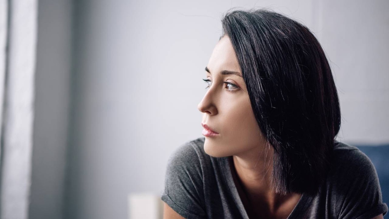 Close-up de perfil de mulher com cabelo escuro e expressão pensativa, olhando para o lado