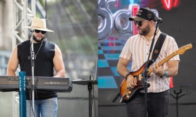 Dois músicos no palco, um tocando teclado, outro guitarra elétrica, durante apresentação