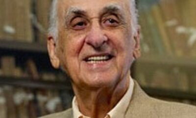 Zuenir Ventura idoso, cabelos brancos, sorrindo, em casaco claro, fundo desfocado