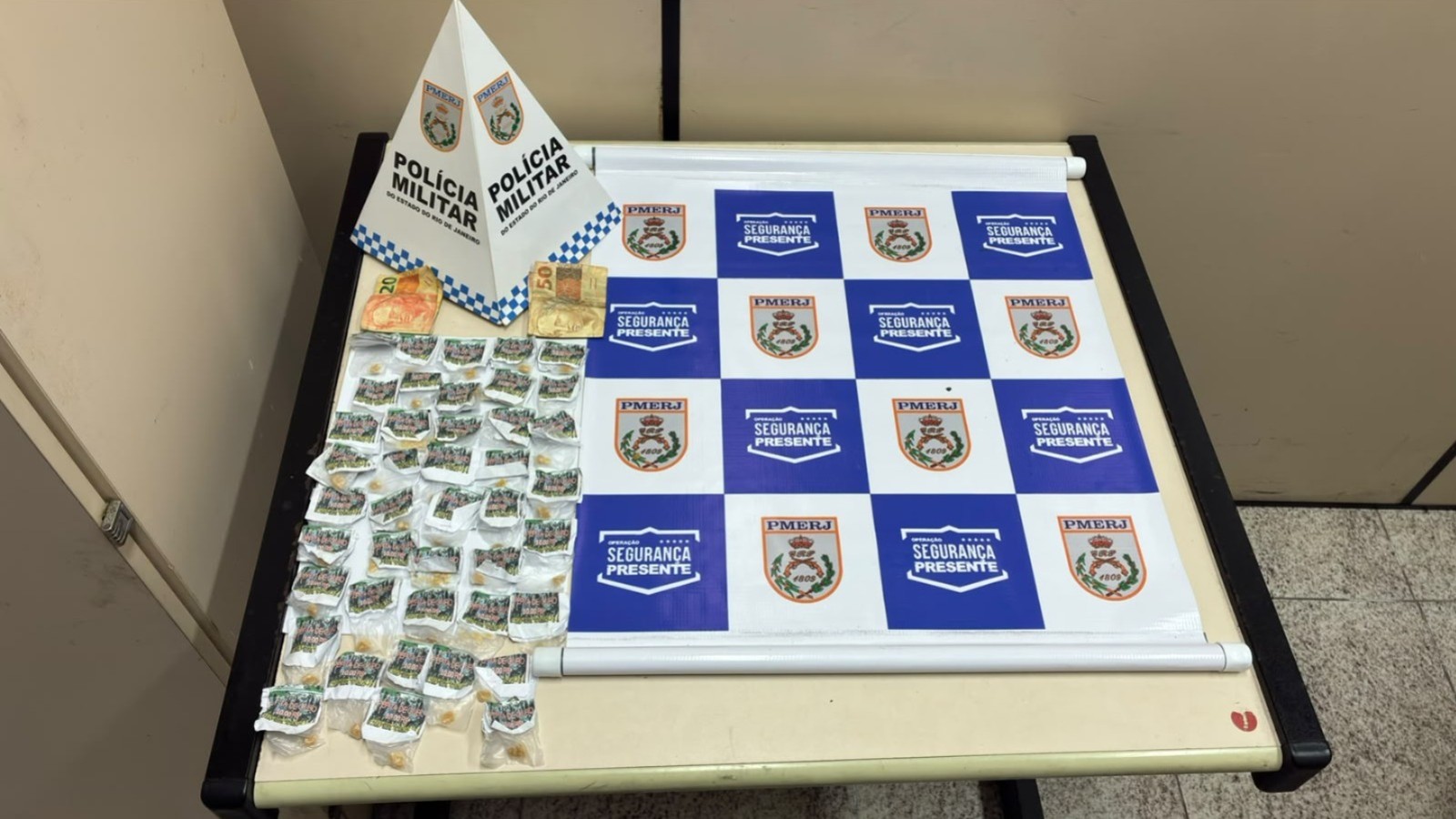 Dinheiro e dezenas de porções de crack em embalagens plásticas sobre uma mesa da Polícia Militar