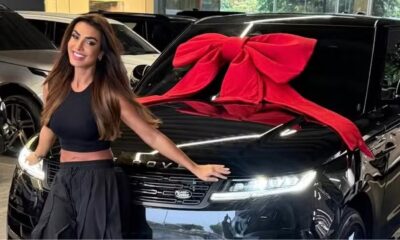 Mulher sorrindo em frente a um SUV preto Range Rover com laço vermelho e logo Land Rover visível