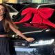 Mulher sorrindo em frente a um SUV preto Range Rover com laço vermelho e logo Land Rover visível