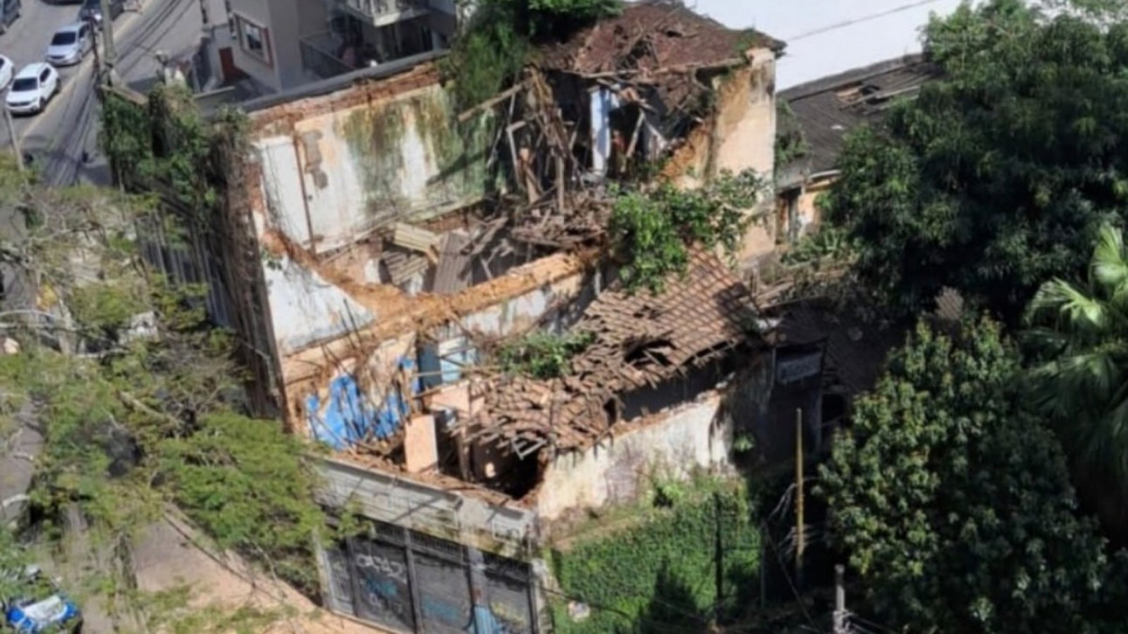 Vista aérea de prédio antigo e parcialmente desabado, com telhado e paredes destruídas e vegetação
