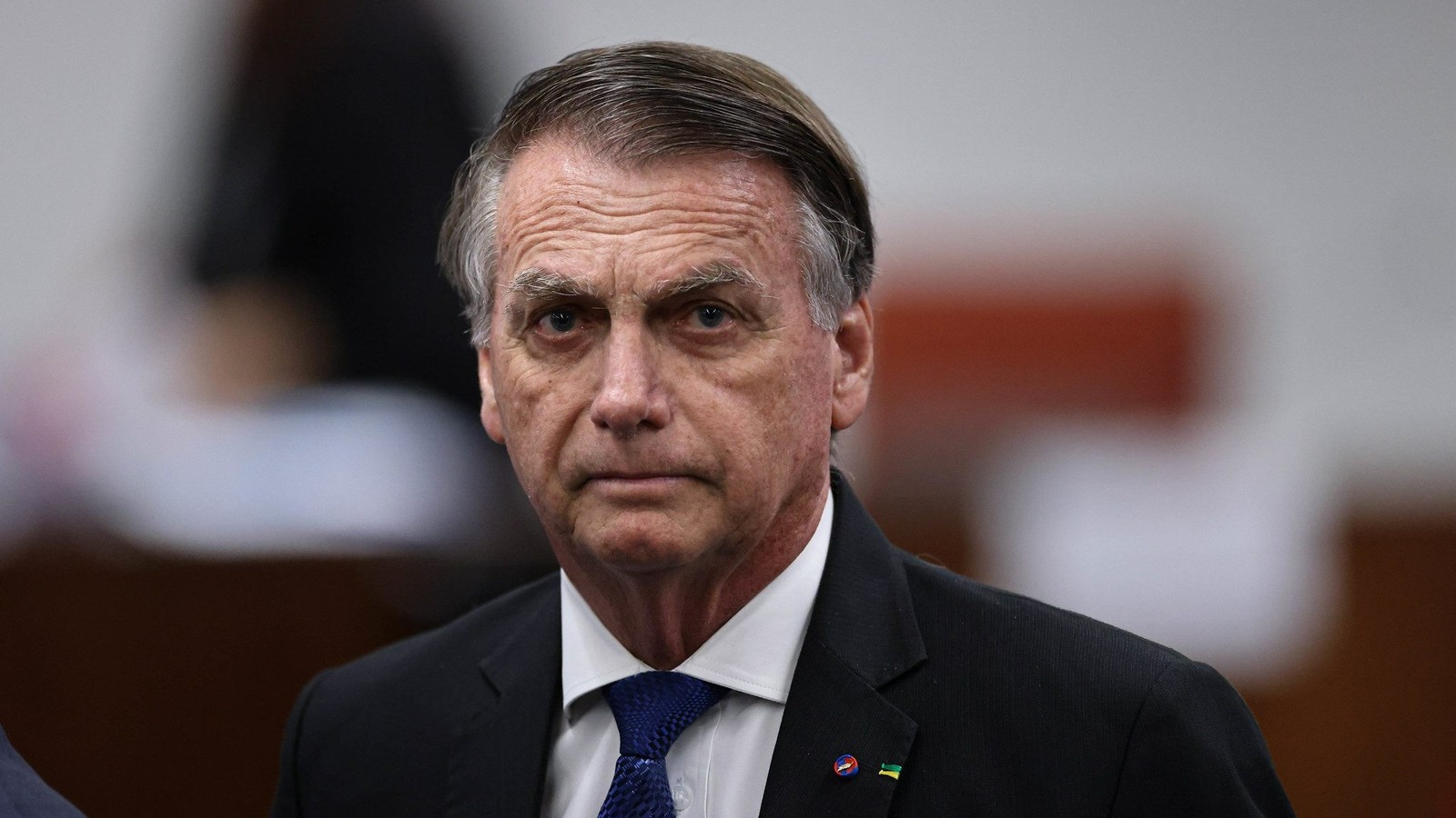 Jair Bolsonaro com semblante sério, usando terno escuro, camisa branca e gravata azul
