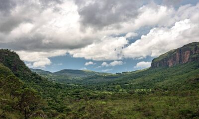 Vasto vale verde com montanhas íngremes, um paredão rochoso e céu dramático com nuvens