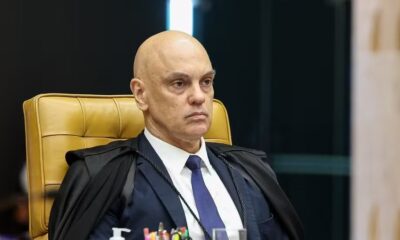 Homem careca de terno azul, gravata azul e toga preta sentado em cadeira amarela