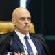 Homem careca de terno azul, gravata azul e toga preta sentado em cadeira amarela