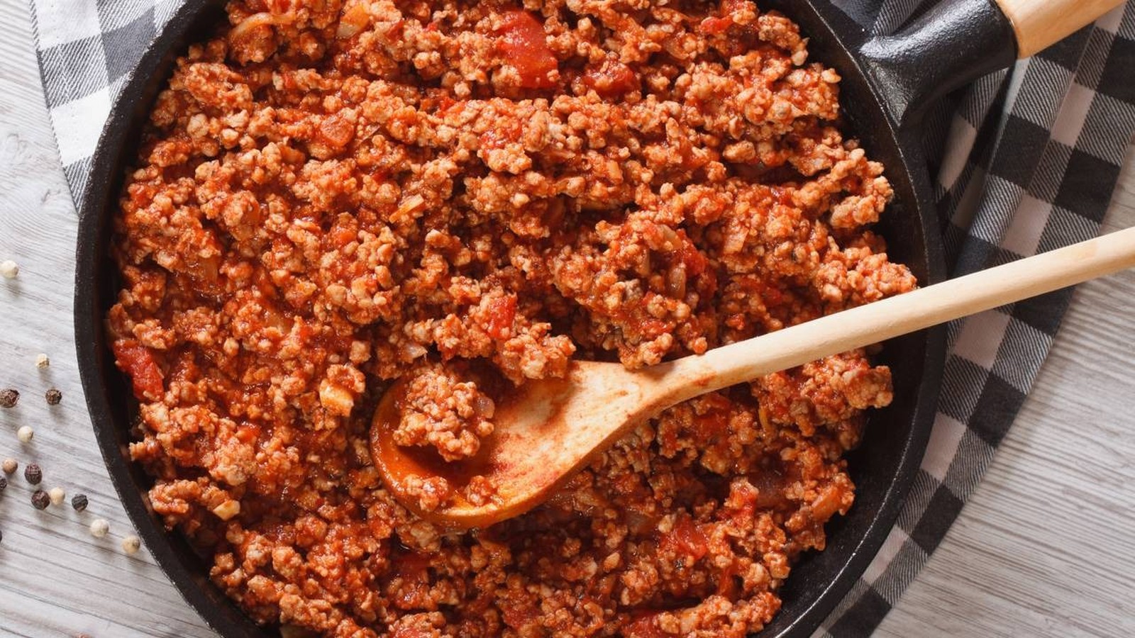 Carne moída refogada em molho vermelho com colher de pau em frigideira preta