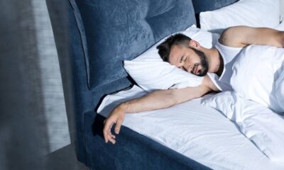 Homem barbudo dormindo profundamente na cama com travesseiro e lençóis brancos