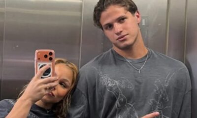 Mulher loira tira selfie com homem de camisa cinza em espelho de elevador