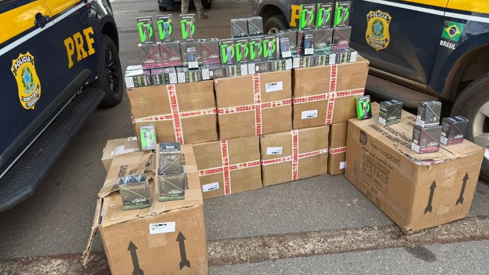 Caixas de cigarros eletrônicos Vaporesso V300 sobre caixas de papelão, ao lado de carro PRF