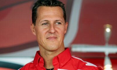 Close-up de Michael Schumacher sorrindo e olhando para o lado, vestindo camisa vermelha com detalhes brancos