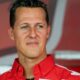 Close-up de Michael Schumacher sorrindo e olhando para o lado, vestindo camisa vermelha com detalhes brancos
