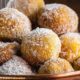 Bolinhos de chuva dourados com açúcar e canela em tigela de cobre, sendo polvilhados