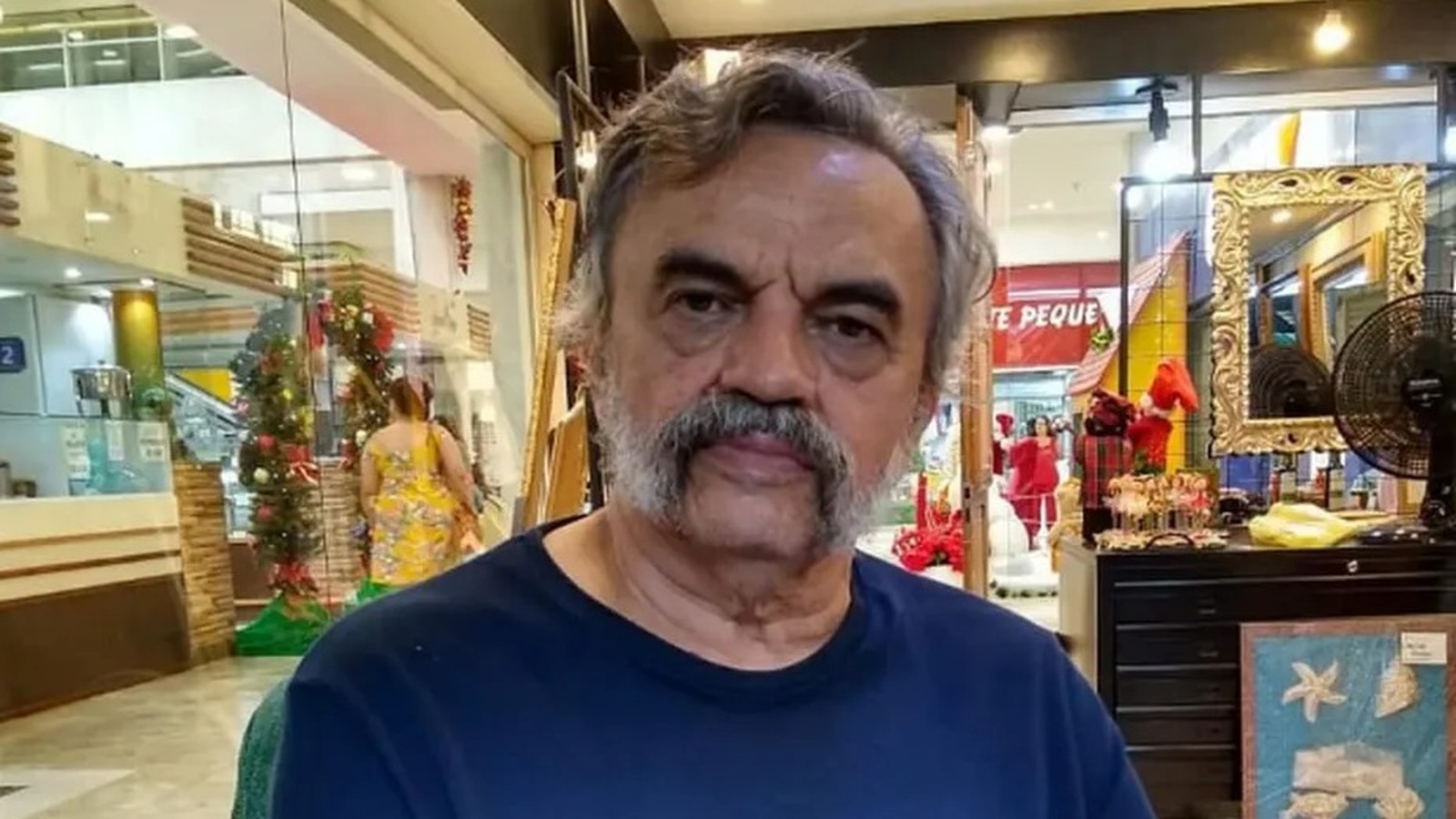 José Dumont, homem de cabelo e bigode grisalhos, vestindo camiseta azul, olhando para frente