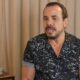 O cantor Ralf, com barba, camisa escura estampada e brinco dourado, falando.