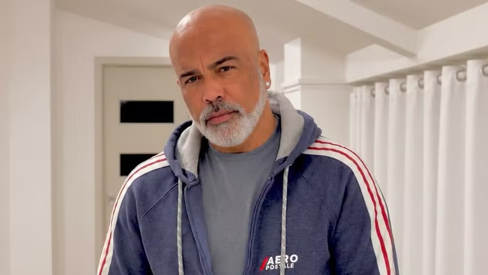 Homem careca e barbudo com camiseta cinza e jaqueta azul Aero Postale