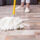 Mop branco molhado no chão de madeira com pessoa limpando