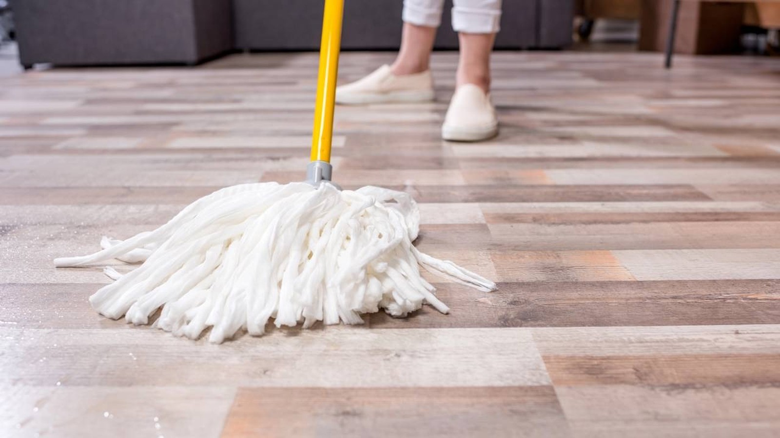 Mop branco molhado no chão de madeira com pessoa limpando