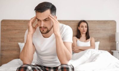 Um homem aflito segura a cabeça enquanto uma mulher chateada vira o rosto na cama