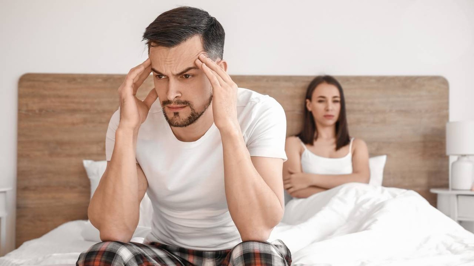 Um homem aflito segura a cabeça enquanto uma mulher chateada vira o rosto na cama