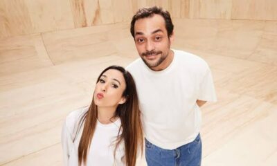 Tatá Werneck de cabelo castanho fazendo bico ao lado de Eduardo Sterblitch sorrindo, fundo de madeira