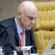 Ministro Alexandre de Moraes de toga olhando para laptop com logo STF