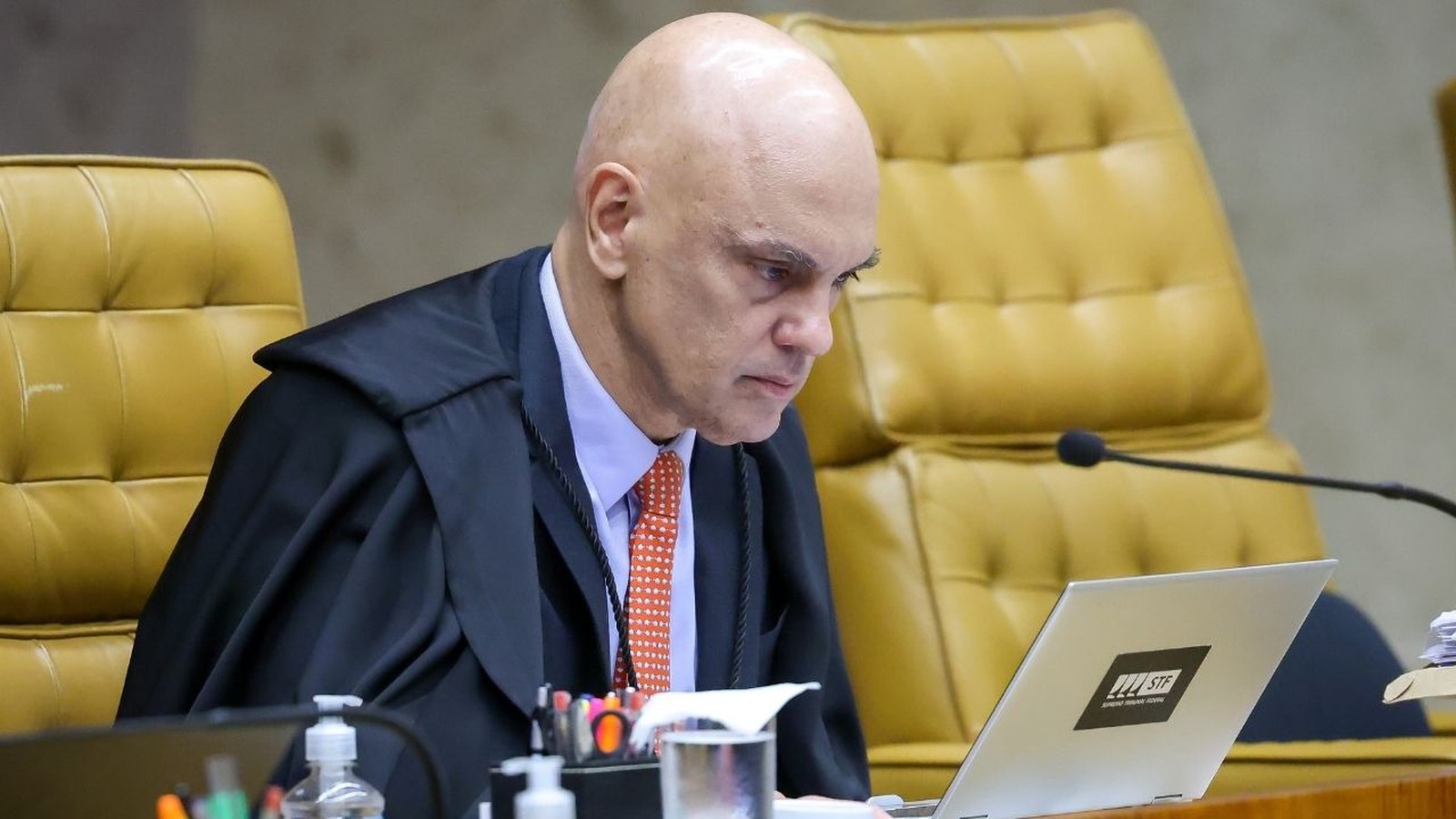 Ministro Alexandre de Moraes de toga olhando para laptop com logo STF