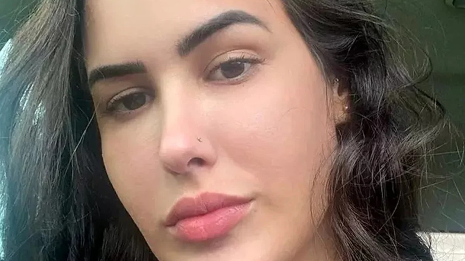 Close-up do rosto de uma mulher com cabelos escuros, olhos castanhos e piercing no nariz