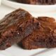 Duas fatias de brownie de chocolate com casquinha rachada e brilhante em prato branco