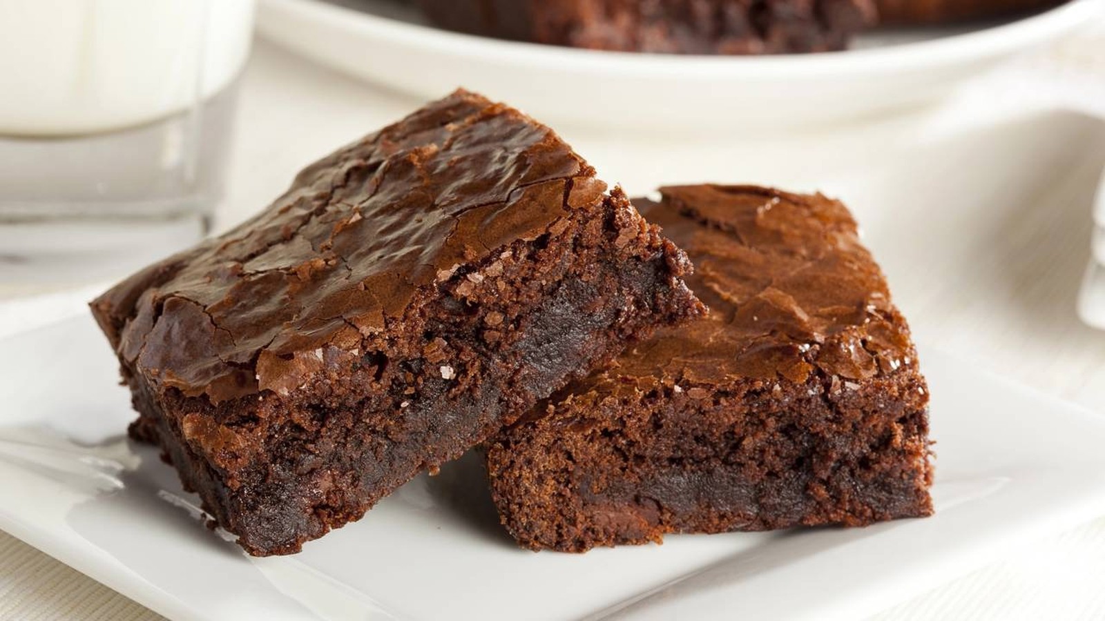 Duas fatias de brownie de chocolate com casquinha rachada e brilhante em prato branco