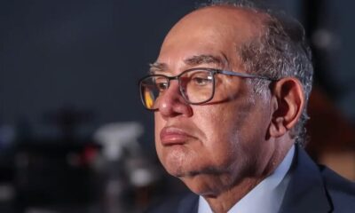 Homem de óculos e terno com cabelo grisalho olhando para o lado direito da imagem