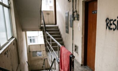 Corredor de edifício com escada, porta 'Apt 302', pichação 'RESIS' e toalha vermelha no corrimão