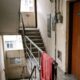 Corredor de edifício com escada, porta 'Apt 302', pichação 'RESIS' e toalha vermelha no corrimão