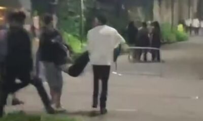 Três pessoas carregam uma figura caída em uma rua escura à noite